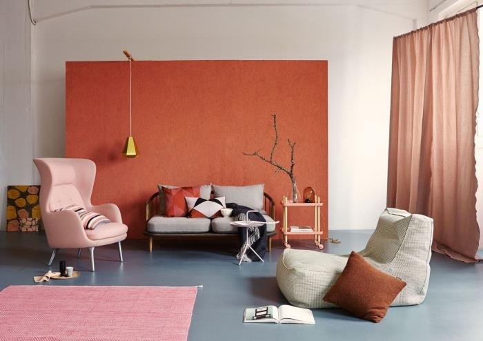 pastelovo ružové kreslo bledoružový koberec terakotová nástenná maľba dekorácia obývačky dlhé terakotové závesy sivý a kovový gauč terakotový vankúš