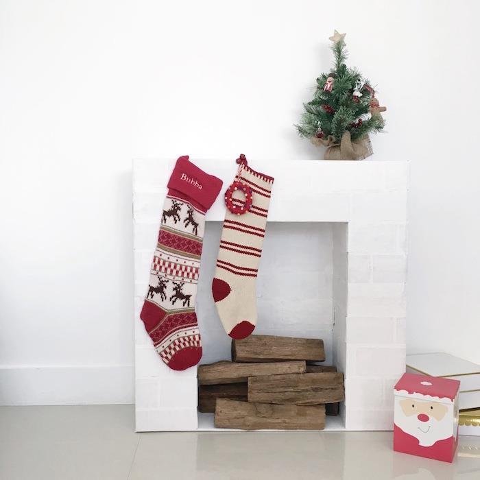 modell små falska dekorativa eldstäder imitation vita tegelstenar på vit vägg med trä stockar och juldekoration med mini gran strumpor
