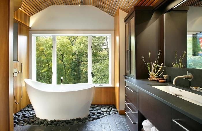 Ázijské usporiadanie kúpeľne s malou voľne stojacou vaňou na záhrade so sivými kamienkami, dekor kúpeľne v sivobielej farbe a dreve