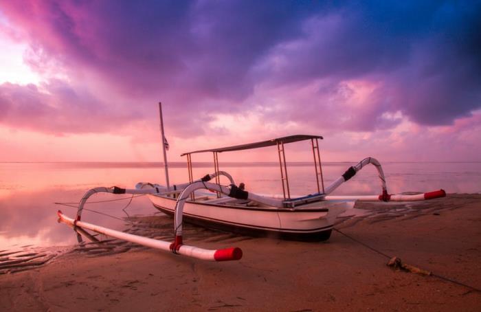 en moderniserad båt vid havet. rosa och lila himmel, lugnt vatten, ljusbrun sand, magiskt ljus