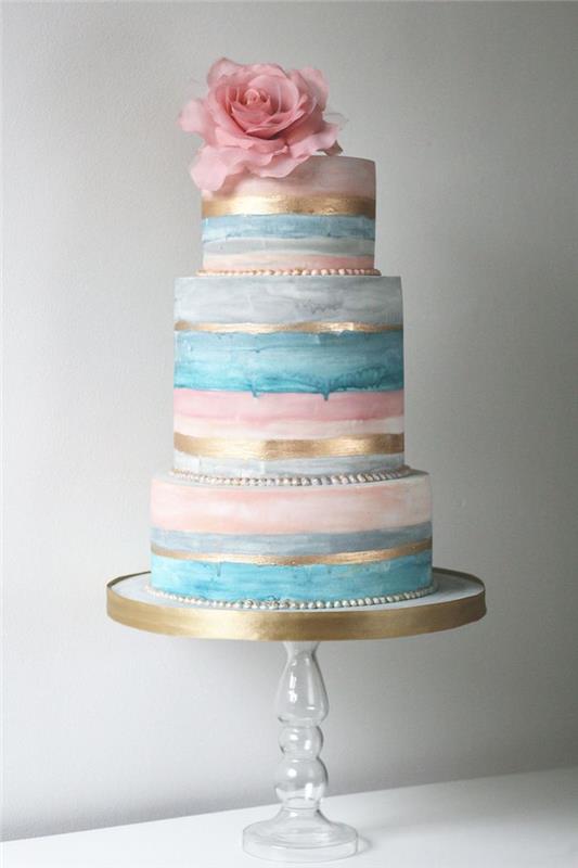 enkel och vacker tårta i grå, blå och rosa färg med guldband och dekoration av färsk rosa blomma ovanpå