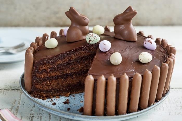 snabb och enkel påsktårta, choklad påsk fudge tårta recept omgiven av fingrar och dekorerad med kaniner och chokladägg