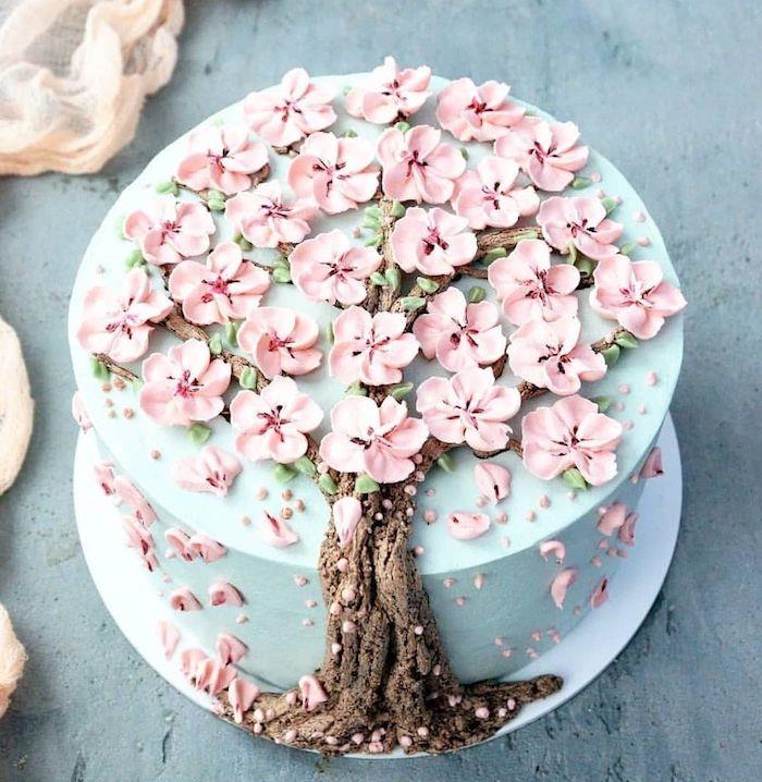 ganska original tårta dekorerad med pastellblå grädde, trädstam i brunt smörkräm och rosa sockerpasta blomblad