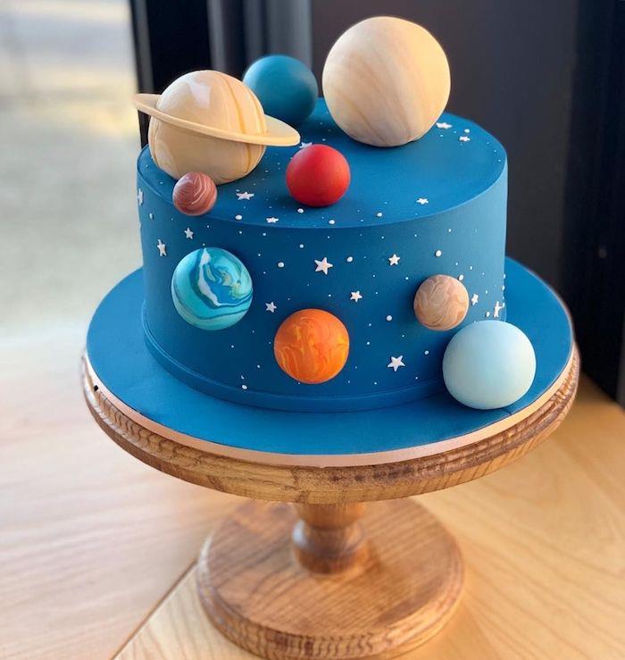 torta zdobená modrou polevou, koláčik planét slnečnej sústavy a ozdobné biele hviezdy