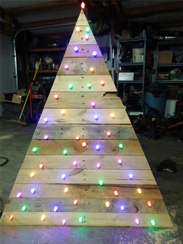 veľký strom vyrobený z paliet, umelý stromček ozdobený malými farebnými svetlami, drevený vianočný stromček