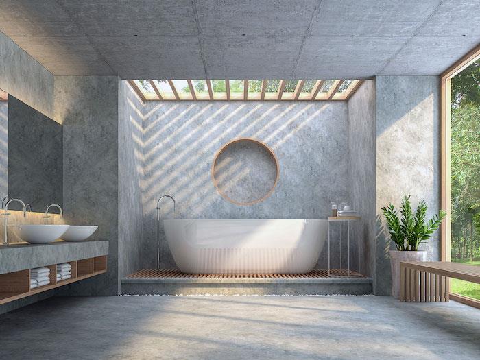 حمام كبير مفتوح مع نافذة كبيرة تطل على الحديقة وجدران خرسانية وأرضية سقف مع حوض استحمام قائم بذاته