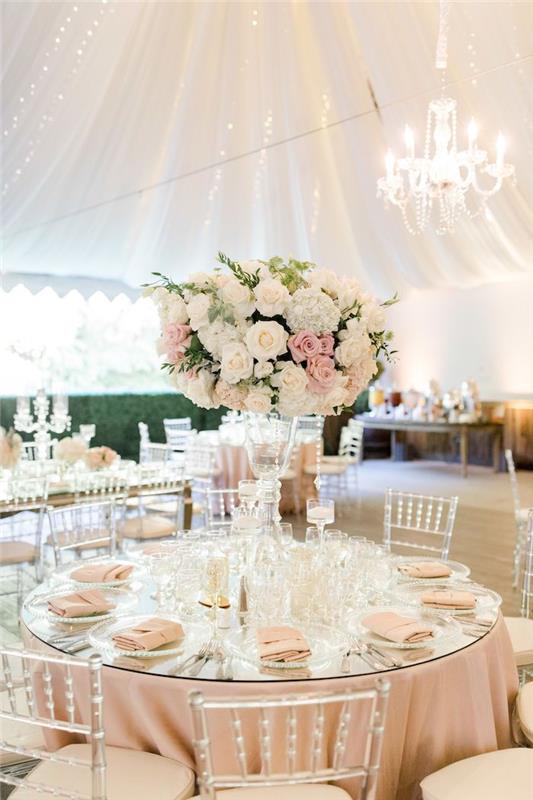 dekorácia svadobného stola v svetloružovom obruse a obrúskoch s veľkým centrom deky s kyticou kvetov, závesnou oblohou, priehľadnými stoličkami