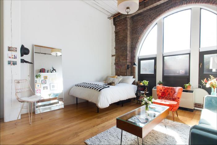 industriloft som dekorerar idé med stora burspråk, tegelvägg, blå soffa, orange fåtölj, hög säng, spegel i mänsklig storlek