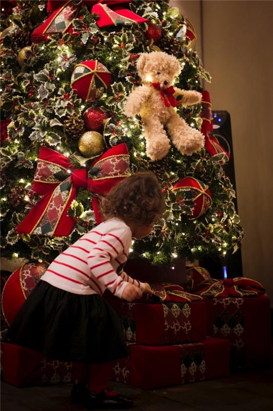 Happy holidays bild för mobil tapet, foto av liten flicka framför ett stort träd dekorerat i rött grönt