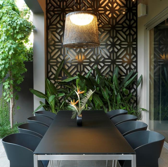dekorácia vonkajšej steny čiernym kovovým panelom so štýlovými kvetinovými vzormi, veľký obdĺžnikový stôl v čiernom pláne s nohami z ľahkého kovu, osem stoličiek s čiernymi chrbtami z PVC, obliekanie vonkajšej steny