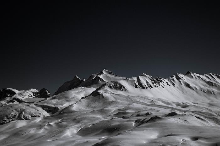 vitheten hos en stenig bergsrygg täckt med snö som sticker ut mot bakgrunden av den svarta himlen, de vackraste bilderna av svartvita bergslandskap