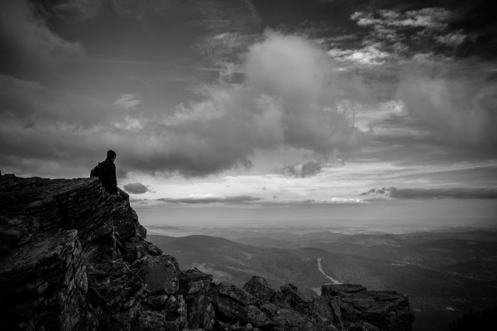 vackert foto av mannen som sitter på en klippa och betraktar naturen under molnens skådespel, svartvitt porträtt av man och berg