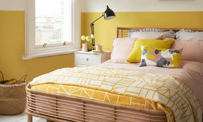 غرفة نوم صغيرة باللونين الأصفر والأبيض ، سرير مع ألحفة وردية وصفراء ، مصباح طاولة بتصميم صناعي أسود