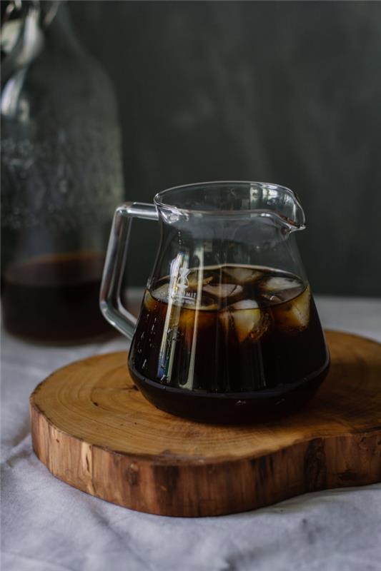 ako pripraviť ľadovú kávu nespresso, recept na studenú čiernu kávu na leto, pohár čiernej kávy s kockami ľadu na drevenom pláte