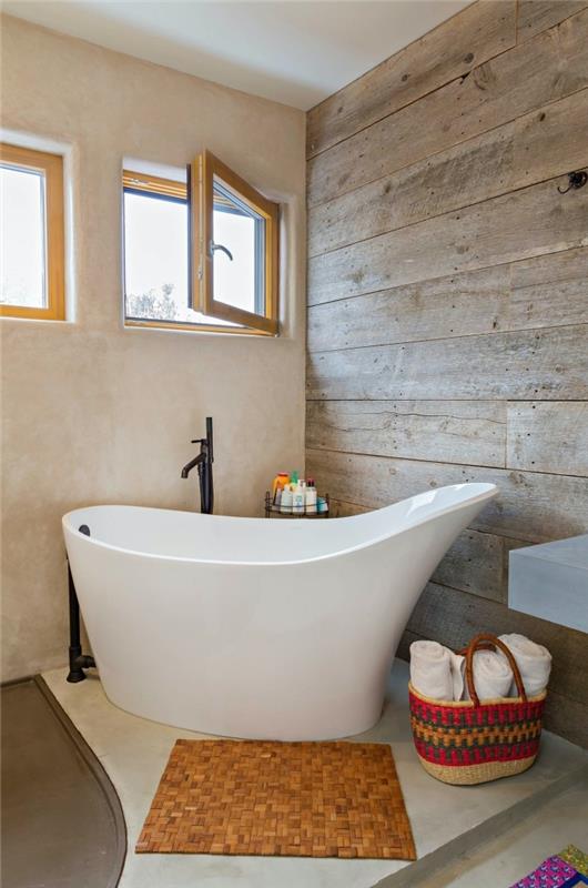 voľne stojaci model bokovej vane v malej kúpeľni s drevenými stenami a podlahou v bielej a šedej farbe