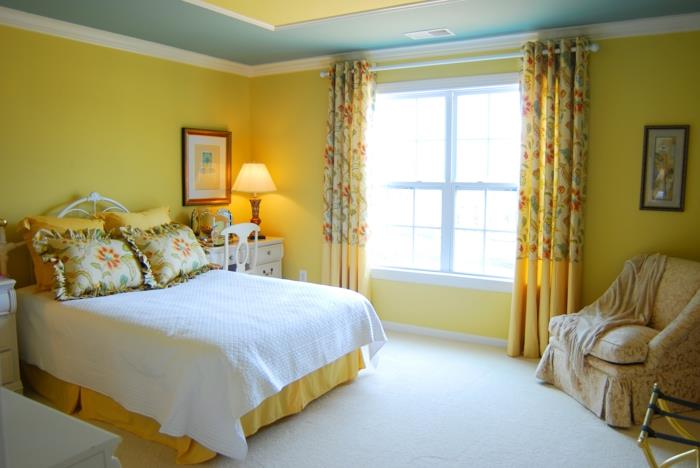 غرفة نوم باللونين الأصفر والأزرق ، وسائد مزخرفة بكشكشة ، وسقف أزرق وأصفر ، وأرضية بيضاء ، وكرسي ستائر كبير بذراعين