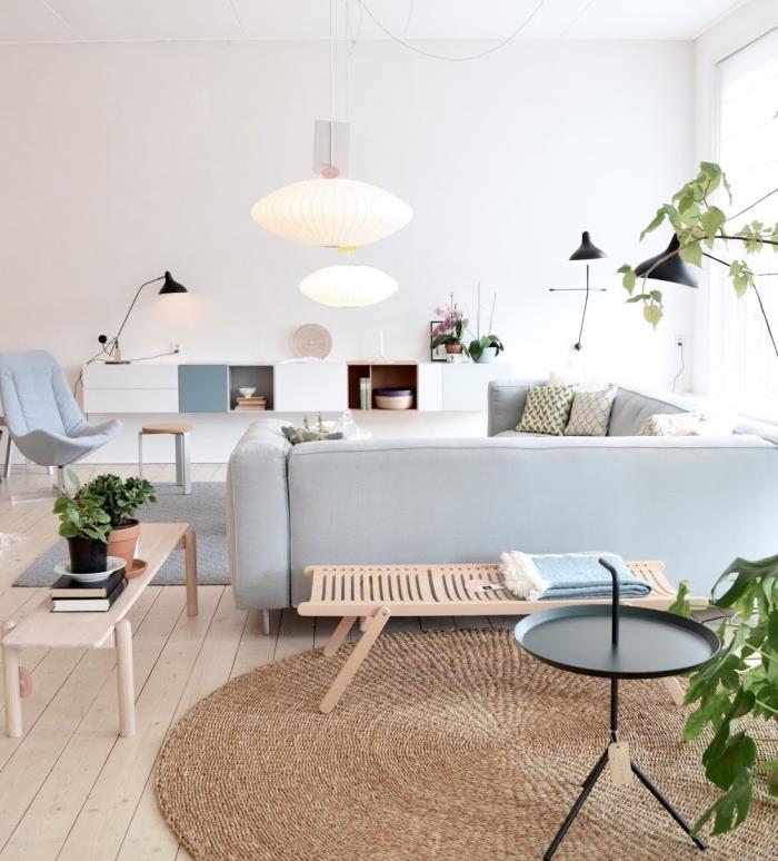 moderné usporiadanie obývačky so sivou sedačkou, sivým škandinávskym kobercom a iným okrúhlym hnedým kobercom, svetlo sivou rohovou sedačkou, svetlými parketami, škandinávskym dreveným nábytkom, bielou skrinkou pod televízor