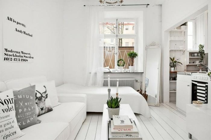 Škandinávsky nábytok v malom bielom štúdiu, biela posteľ a sedačka, svetlé parkety, biely konferenčný stolík, biela kuchynská fasáda, zelené rastliny, čiernobiely citát plagát
