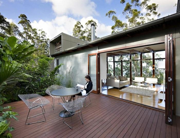 modernt vardagsrum som vetter mot en zen -terrass i brunt kompositträ, designbord och stolar, gränsen till gröna växter