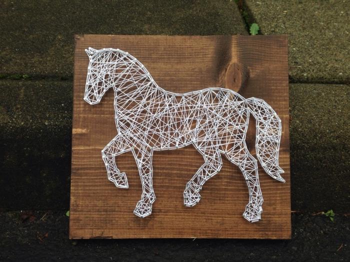 vacker DIY väggdekoration gjord med en mörk träskiva och en vit tråd lindad runt naglar i form av en häst