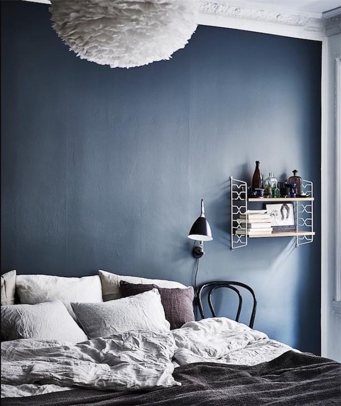 Dekor spálne pre dospelých v tmavo modrej farbe ako farba na stenu, sivá posteľná bielizeň, polička v retro štýle, biele závesné svetlo