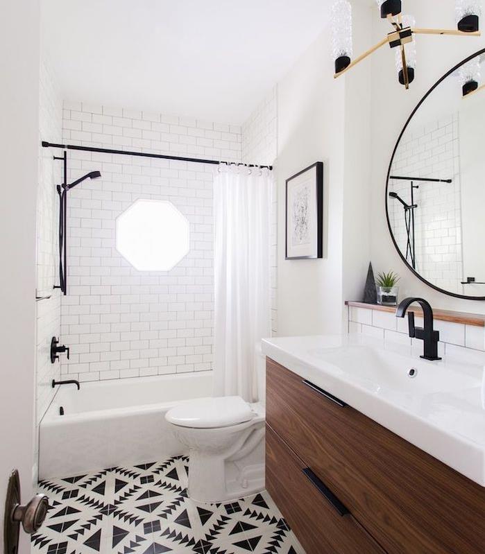 malá drevená kúpeľňová skrinka s bielym umývadlom, veľké okrúhle zrkadlo, vaňa so sprchovým závesom, čiernobiele dlažby