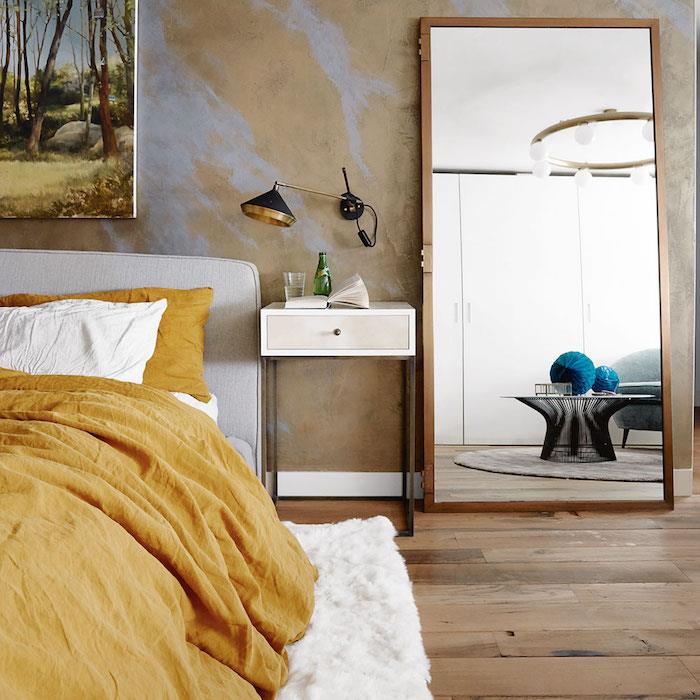 nápad vyzdobiť svoju izbu, parkety zo svetlého dreva, bielu a horčicovožltú posteľnú bielizeň a mäkký koberec, žltú stenu s purpurovými čipmi, veľké zrkadlo s dreveným rámom