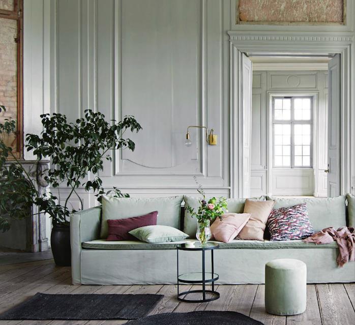 celadon zelená obývačka v bielej farbe na stenu a sivozelená sedačka, hnedé parkety, zelená rastlina, ružová, bordová, zelené a farebné vankúše, minimalistický čierny stôl