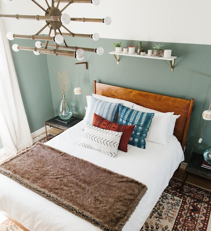 dizajnová spálňa so stenami z farebného zeleného dreva, ako čelo postele, originálny luster, drevená posteľ s bielou posteľnou bielizňou, modrými, červenými a bielymi vankúšmi, orientálny koberec, úložný priestor na biele poličky pre malé rastliny