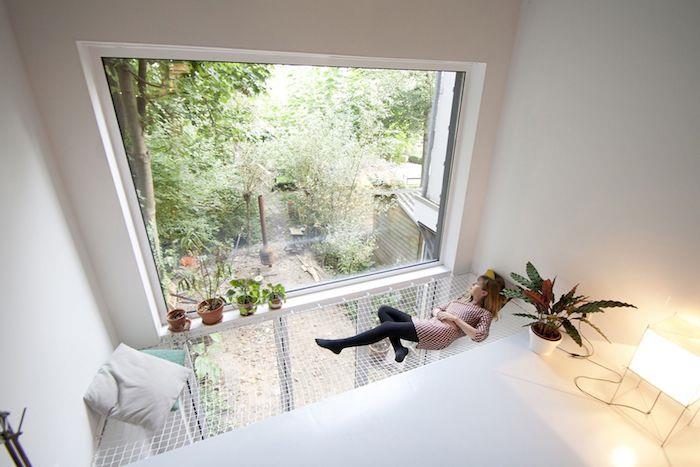 minimalistické deco v bielej farbe s originálnou vnútornou hojdacou sieťou s výhľadom von veľkým oknom, okolo zelené rastliny