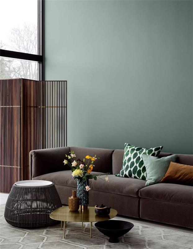 celadon zelená dekorácia obývačky, sedačka uhlovo šedá. zelené a svetlohnedé vankúše, zlatý konferenčný stolík, kovová zástena, kytica kvetov