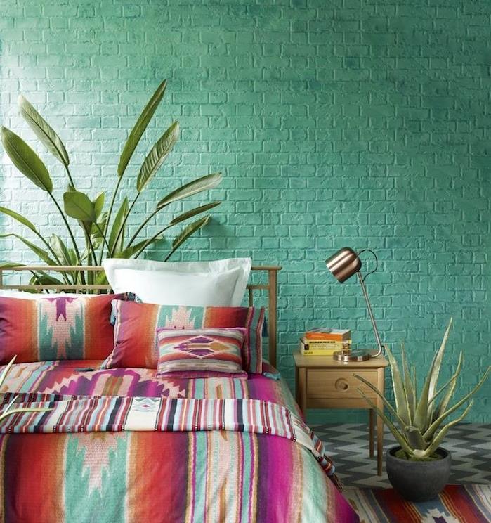 farba spálne pre dospelých, tehlová stena premaľovaná na zelenú, bohémska elegantná posteľná bielizeň s farebnými vzormi, sivá a biela podlahová krytina, dizajnérska lampa, zelené rastliny