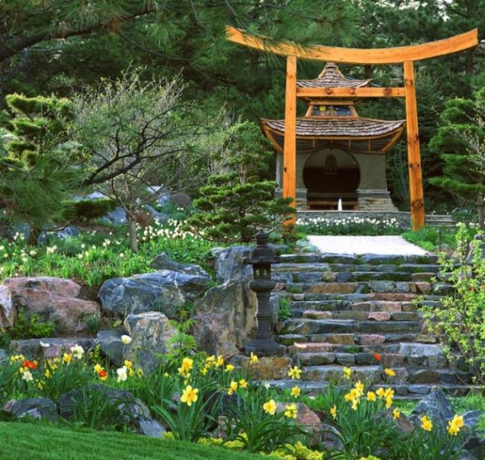 فكرة حديقة زن مجاورة لمعبد ياباني ، درج حجري ، محاط بالحجارة الكبيرة والعشب والزهور النضرة
