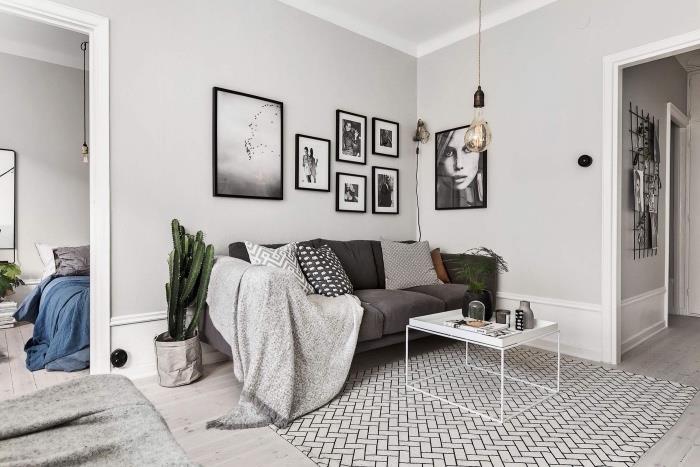 Škandinávsky dekor do obývačky, biely a čierny koberec s geometrickými vzormi, šedá sedačka, svetlo šedá deka, grafický dekor, čiernobiele rámy, svetlé parkety, dekorácia rastlín