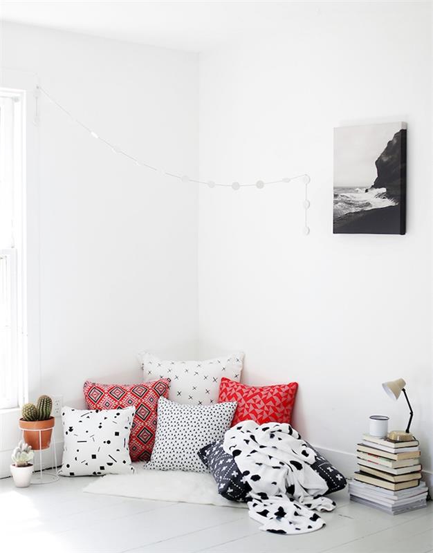 nápad na výzdobu bielej obývačky s priestorom na čítanie na podlahe na bielom koberci farebné vankúše stoh kníh na podlahe a kaktus v kvetináči