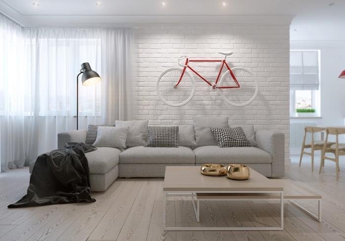 Škandinávsky nábytok do obývačky, sivá sedačka, svetlé parkety, drevené a kovové hniezdne stolíky, svetlé parkety, biela tehlová stena, červeno -biela dekorácia steny na bicykel