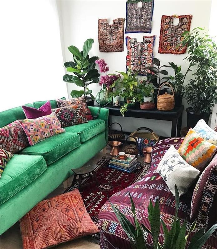 Nápad na tropickú obývaciu izbu so zelenou pohovkou a bordovou pohovkou zdobenou orientálnymi vankúšmi, orientálnymi ozdobnými obloženými stenami, zelenými rastlinami na podlahe a na čiernom servírovacom stole