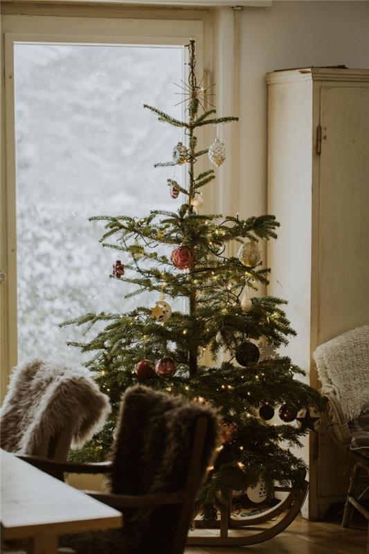 Julbild 2019 med ett naturligt träd dekorerat med ornament och ljus krans i ett vardagsrum med fuskpälsstol