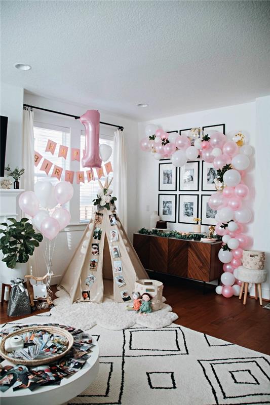 bohemisk chic barns födelsedagsdekoration med tipi i vardagsrummet, en båge av rosa och vita ballonger, aluminiumnummerballong och ett grattis på födelsedagen 1 års banner