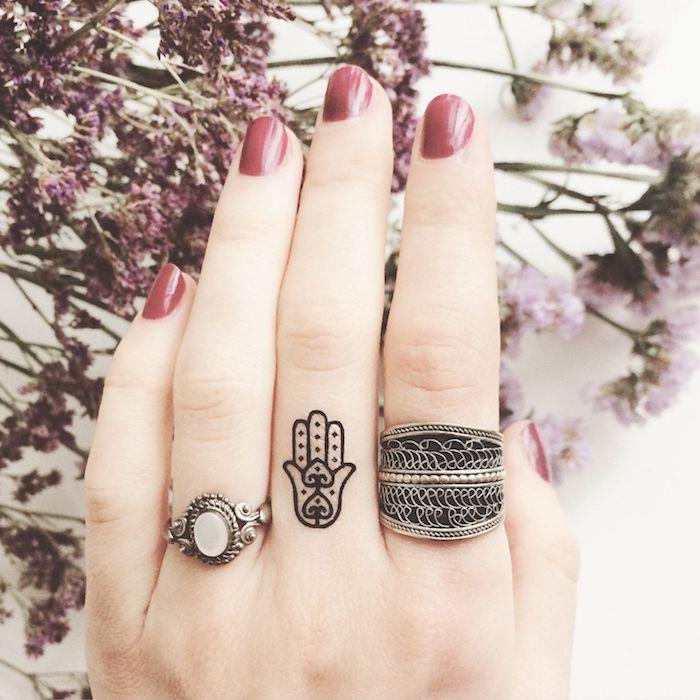 Tatuaggi piccoli mani e un'idea con la mano di fatima disegnata sul dito medio di una donna