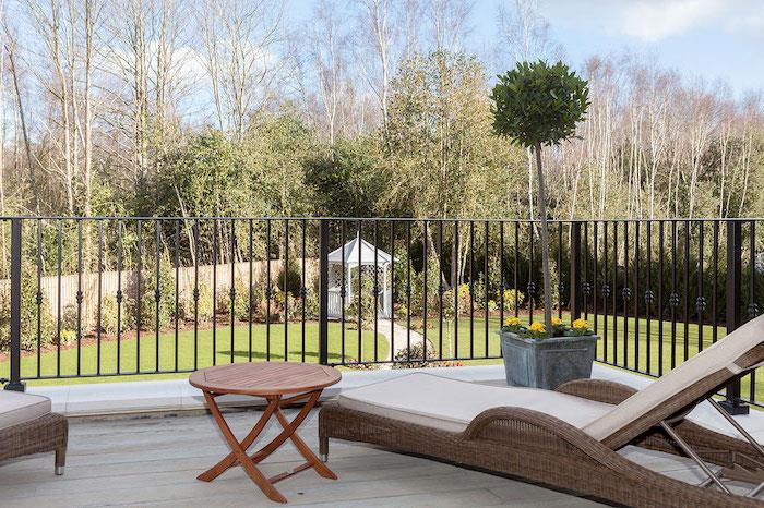 möblera din terrass, grå rotting fåtölj, ljust trägolv, brunt trä soffbord, grönt kronträd, utsikt över en trädgård