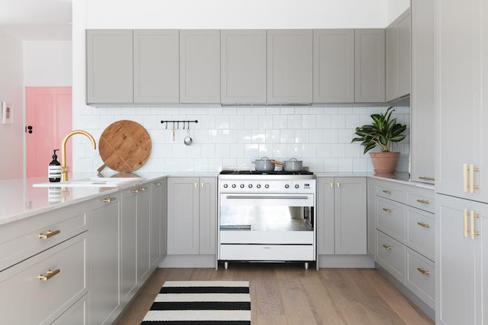 förslag på hur du kan måla om ditt kök i grått, guldhandtag, vita kakelplattor och rosa dörr, svartvit matta