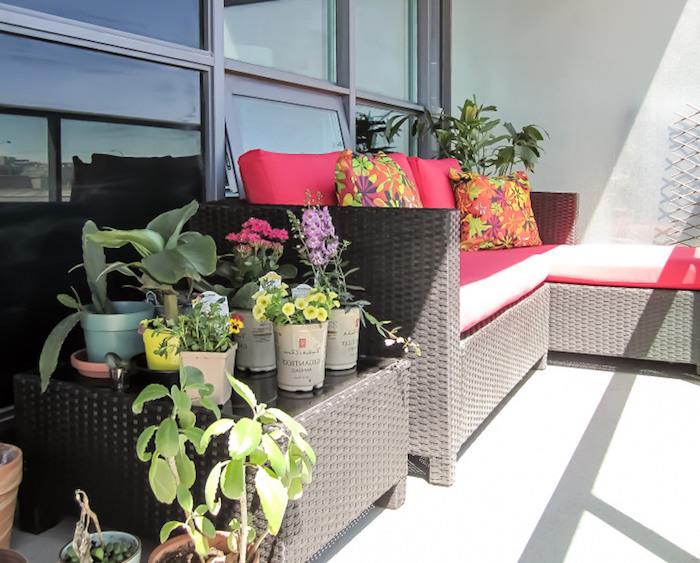 vit uteplatsidé med rottingsoffa och serveringsbord, vävt vardagsrum, rosa sittdynor och färgglada dekorativa kuddar, gröna växter