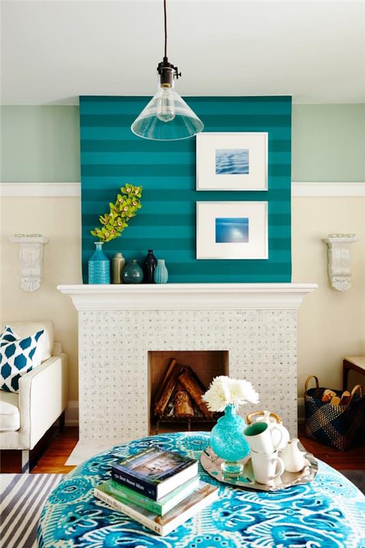 زخرفة الموقد مع رف أبيض عريض تحت جدار أزرق مخطط وإطارات بيضاء مع صور المحيط ، طاولة غرفة معيشة مستديرة باللونين الأزرق والأبيض