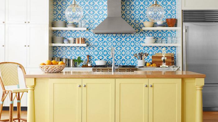 måla om köksskåp, exempel centralö ommålad i gult, skräddarsydda kakelplattor med vita och blå klistermärken, bänkskiva i trä, vita hyllor, bollhänglampor