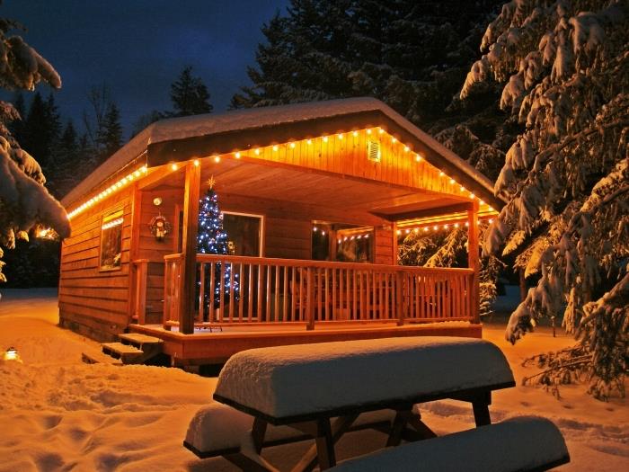 kokonová vianočná tapeta so zasneženou drevenou chatkou a ozdobeným vianočným stromčekom, nočná fotografia domu v zasneženej hore
