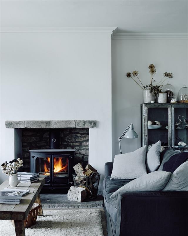 Rustik chic grå vardagsrumsinredning med industriella detaljer med en insats i en öppen spis, ett rustikt träbord och en mjuk grå soffa