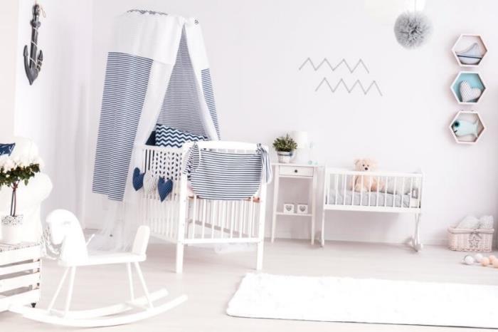 dekor detskej izby s bielymi stenami s bielou a tmavomodrou postieľkou, dekoratívnymi predmetmi v bielej farbe a dreve