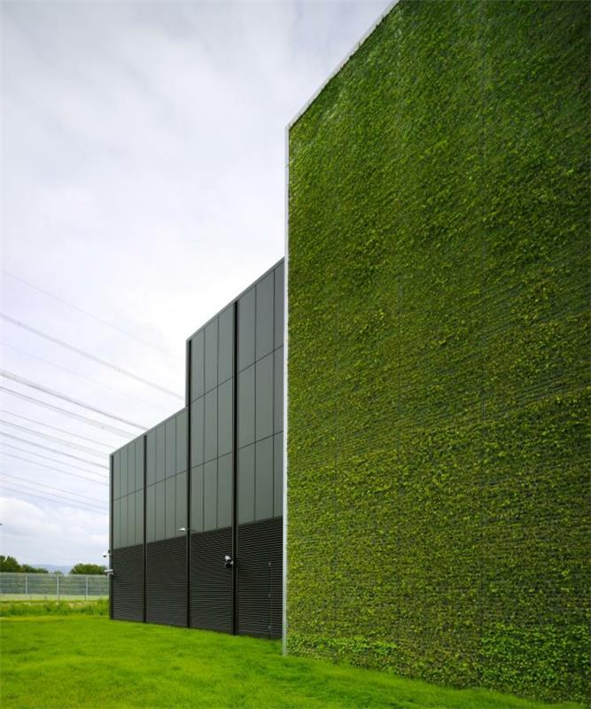 priemyselná budova s ​​vonkajšou zelenou stenou, časť budovy je v čiernych kovových a čiernych oknách, veľké zelené pole