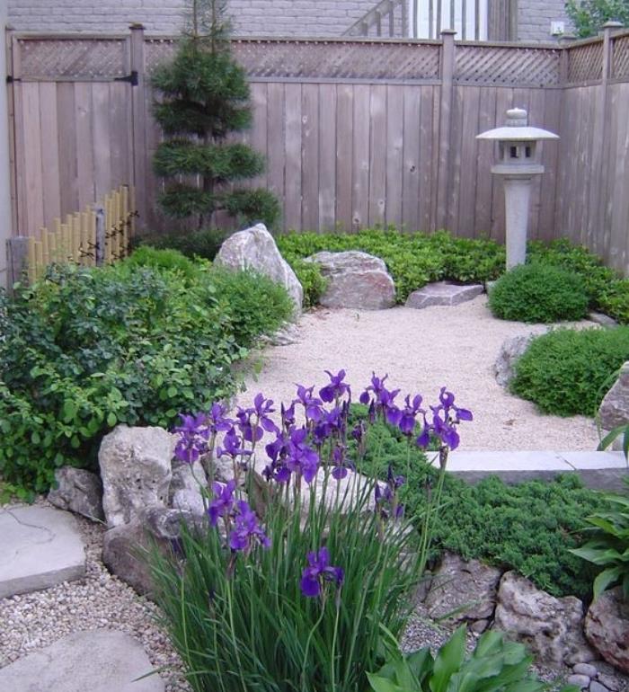 فكرة ركن حديقة زن يابانية صغيرة في الفناء ، ساعة رملية بالحجارة ، شجيرات ونباتات تغطي الأرض ، أزهار أنيقة